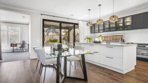A modern kitchen with a glass dining table, white cabinetry, and wooden flooring. - Werribee Luxe Home Family 6Bed Netflix (Werribee)