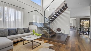 A modern living room with a grey sofa, a coffee table, and a staircase with glass railings. - Werribee Luxe Home Family 6Bed Netflix (Werribee)