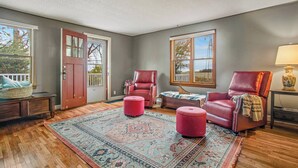 A room with a wooden floor, a red door, a large window, a red leather chair, a small ottoman, and a patterned rug. - Escape To The Countryside At Black Oak Farm (Mount Carroll)