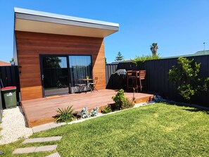 A modern house with a wooden deck, a sliding glass door, and a small patio area with outdoor furniture. - COVE STUDIO1- A perfect mix of comfort and convenience (Hallett Cove)