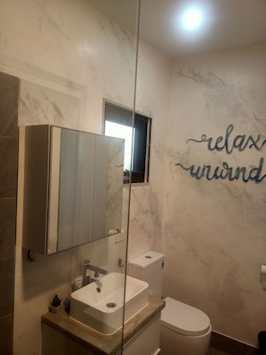 Un bany amb paret de marbre, un lavabo, un vàter i un mirall.