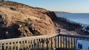 A wooden boardwalk leading to a rocky shoreline with a clear view of the ocean.