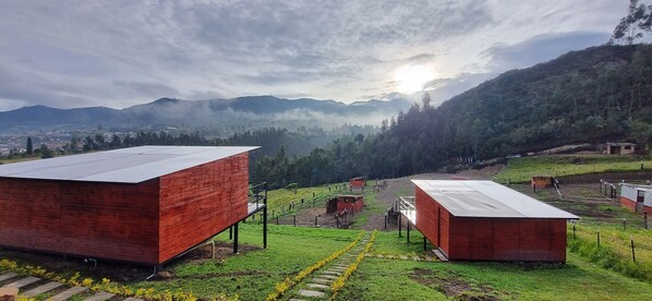 Un paysage rural avec deux bâtiments aux toits rouges, un sentier en pierre et une vue sur des montagnes lointaines.