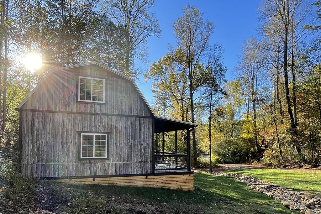 A rustic wooden cabin with a porch, surrounded by trees and a clear sky.