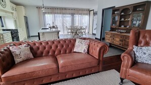 A living room with a brown leather sofa, a wooden armchair, and a dining area with a table and chairs. - Enjoy our Wee Gem, she is over 120 years young and has been loving restored. (Albany)