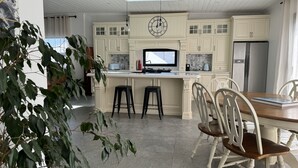 A kitchen with white cabinetry, a central island with stools, a dining table with chairs, and a refrigerator. - Enjoy our Wee Gem, she is over 120 years young and has been loving restored. (Albany)