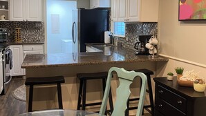 A modern kitchen with white cabinets, a black refrigerator, and a tiled backsplash. There is a dining area with a glass table and chairs, and a decorative bowl on the table.