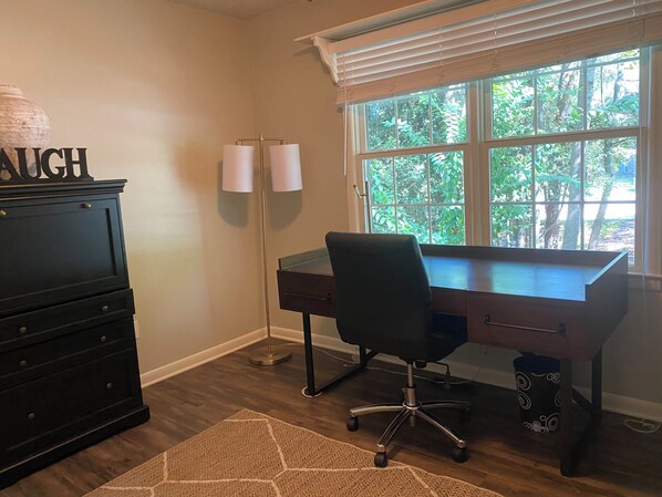 A room with a desk, a dresser, and a window with blinds.