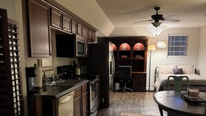 A kitchen with dark wooden cabinets, a microwave, and a refrigerator. There is a dining area with a table and chairs, and a ceiling fan above.