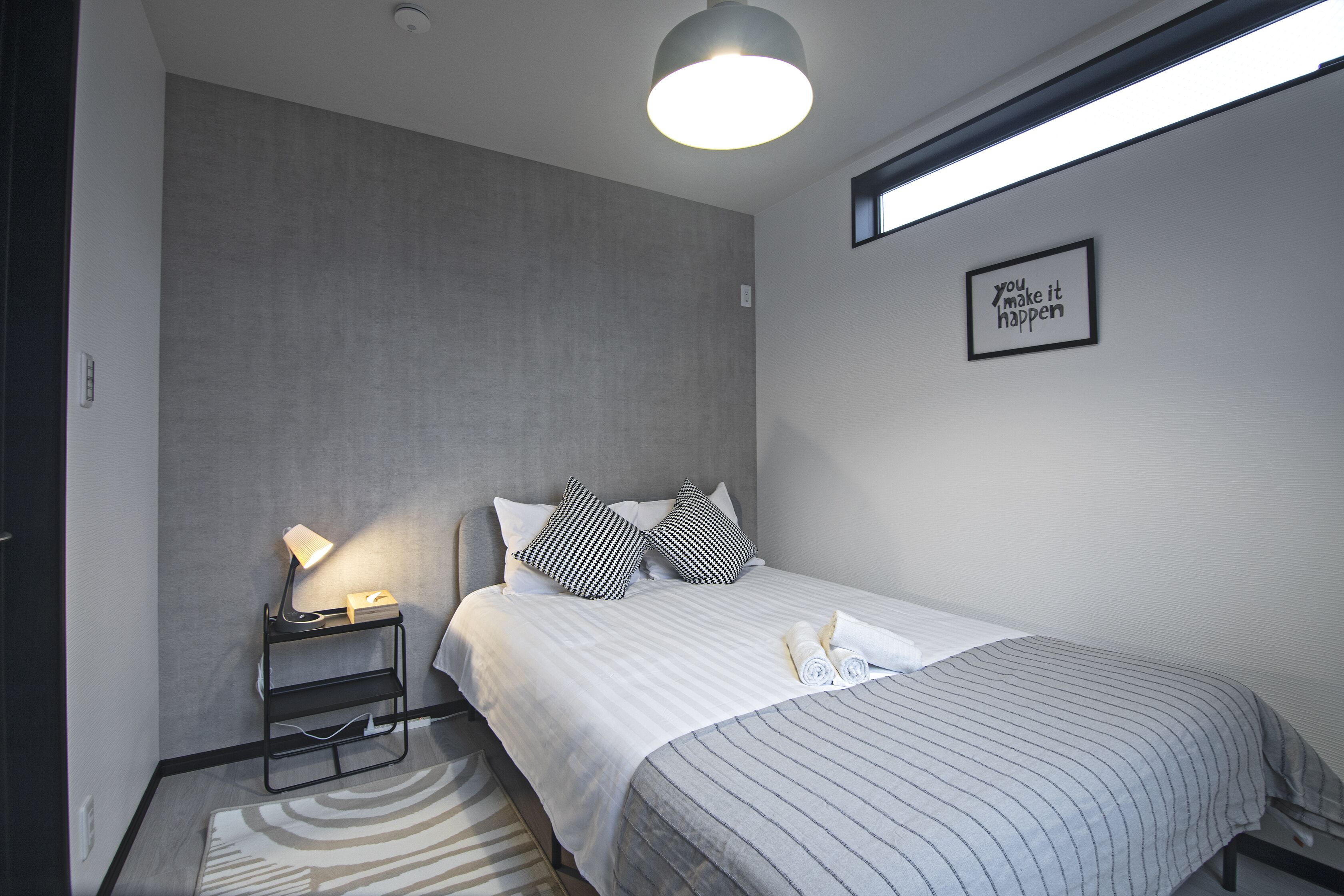 Ein modernes Hotelzimmer mit einem Bett, einer Nachttischlampe und einem motivierenden Zitat an der Wand.