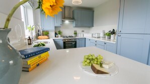 Een moderne keuken met blauwe kastjes, een wit aanrecht en een centraal kookeiland met een presentatie van kaas en druiven.