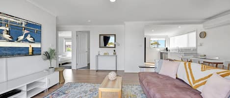 Una sala moderna con un sofá, una mesa de centro y un televisor. Cuenta con una zona de cocina con una mesa y sillas para comer.