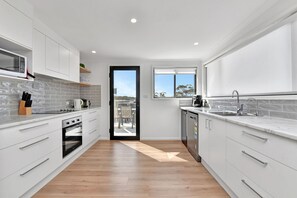 A modern kitchen with white cabinetry, a built-in oven, a microwave, and a window providing a view of the outdoors.