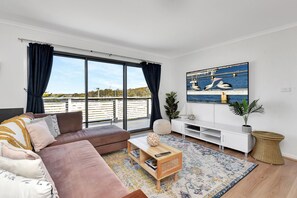 A modern living room with a large window, a sofa, a coffee table, a TV, and a plant.