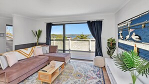 Un salon moderne avec un canapé, une table basse et une vue sur la mer grâce à de grandes fenêtres.