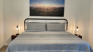 A bedroom with a bed, a ceiling fan, a nightstand with a lamp, and a wall-mounted picture.