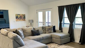 A modern living room with a sectional sofa, a rug, and a large window with curtains.