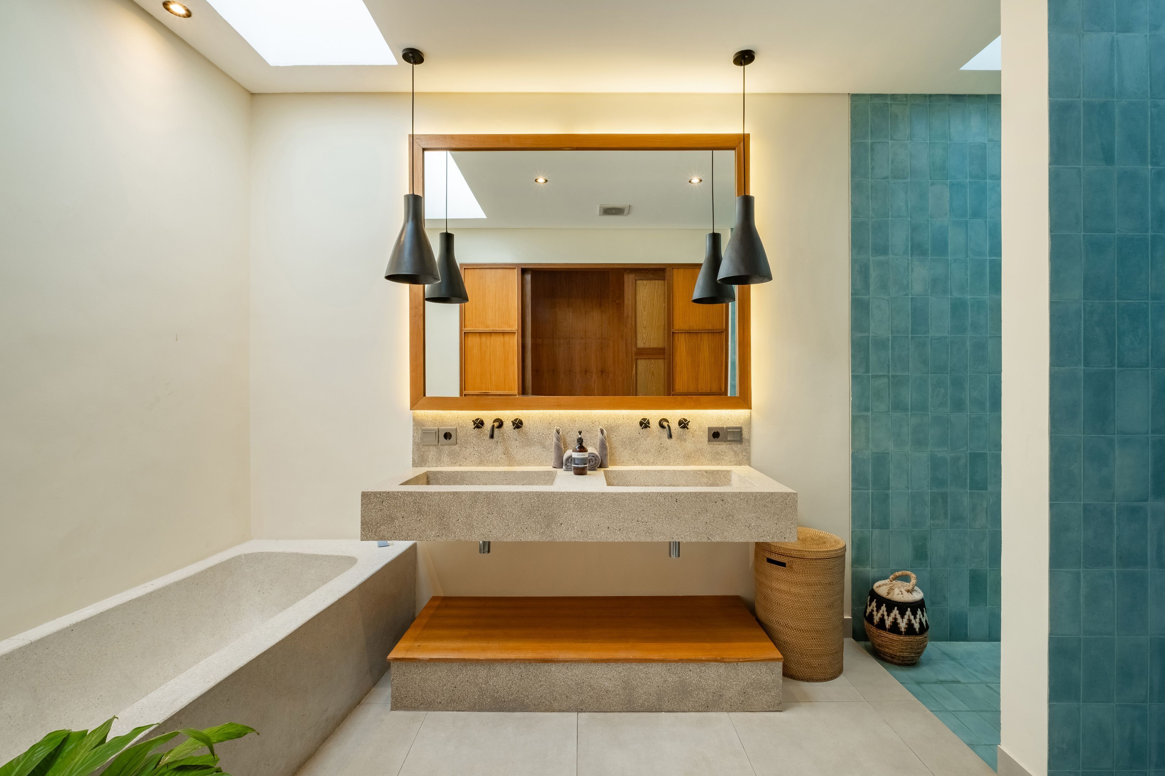A modern bathroom with a large mirror, two pendant lights, a bathtub, and a sink with a wooden shelf.