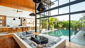 A modern interior with a large glass wall, a pool, and a wooden ceiling. - Villa Gaia Pererenan (Canggu)