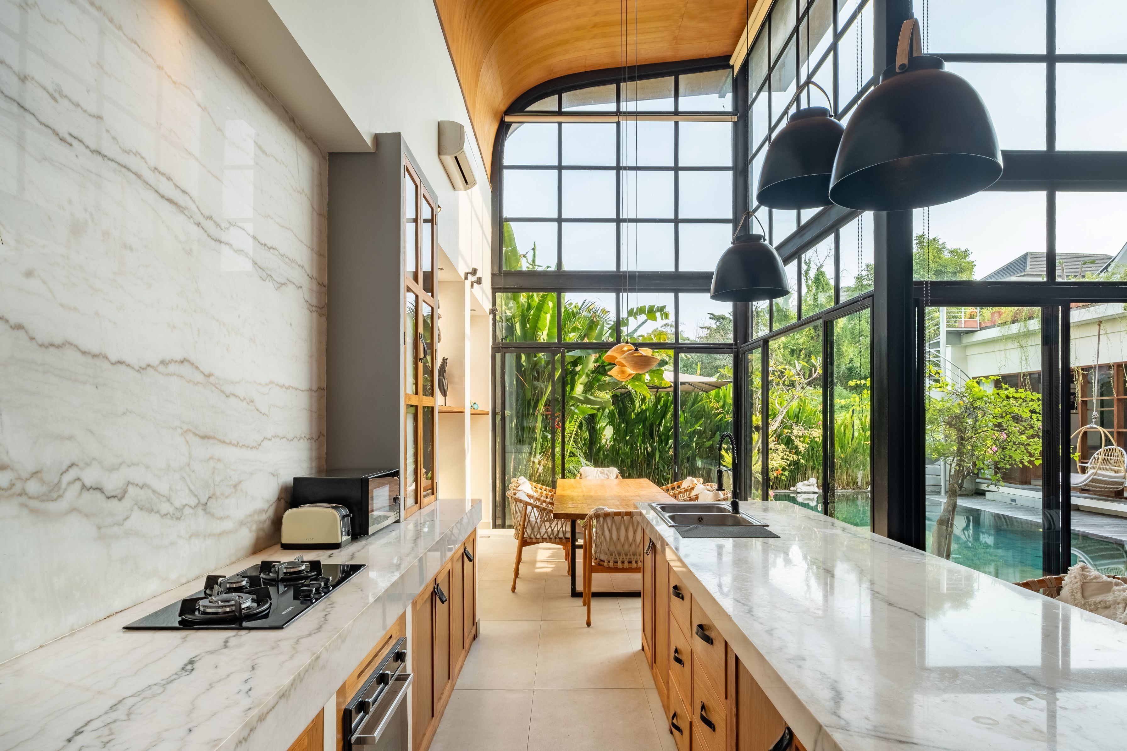 Una cocina moderna con encimeras de mármol, armarios de madera y vistas a una piscina.