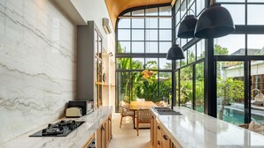 A modern kitchen with marble countertops, wooden cabinets, and a view of a swimming pool. - Villa Gaia Pererenan (Canggu)
