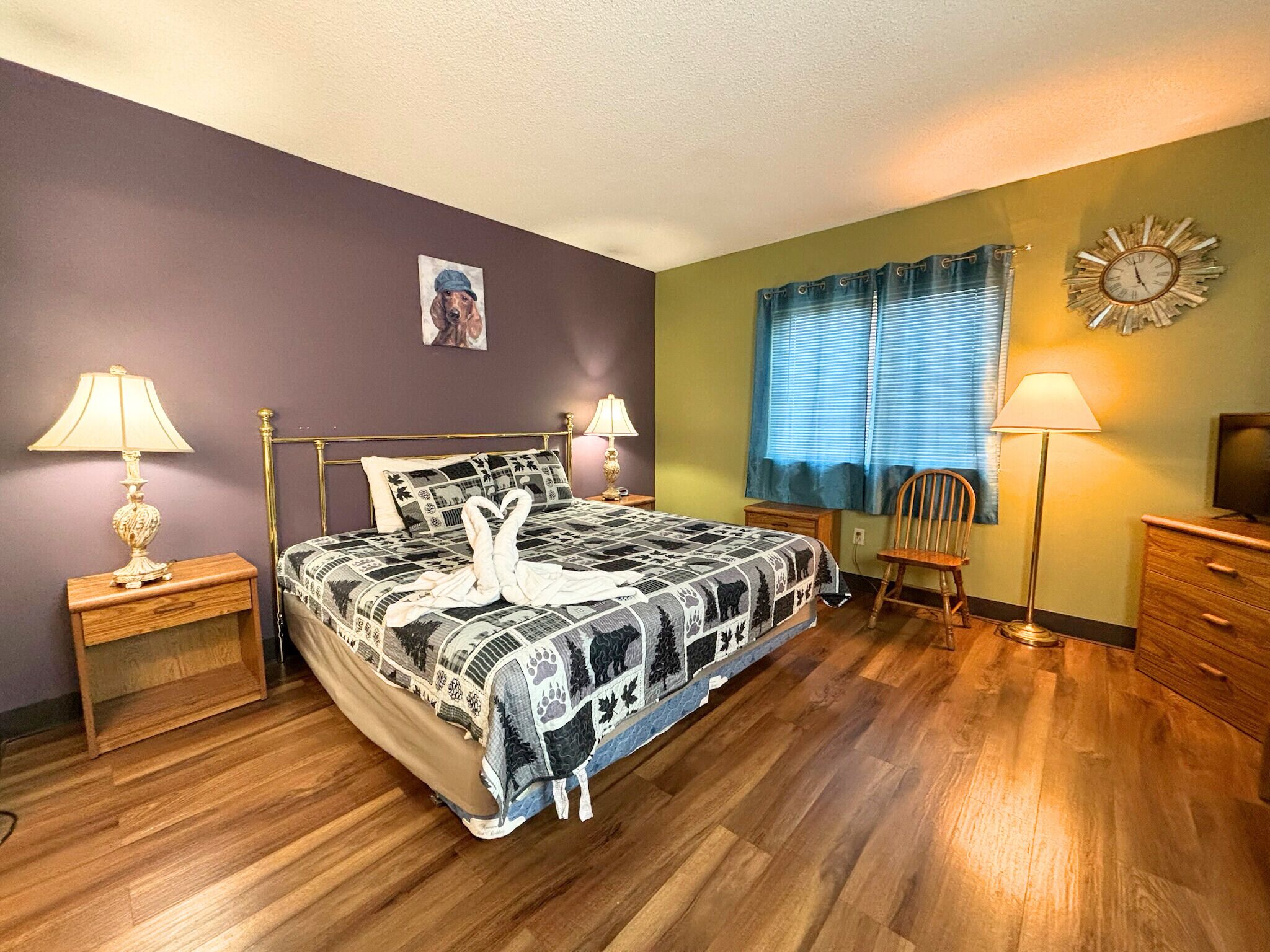 Una camera da letto con un letto, due comodini, una sedia, un mobile TV e una sveglia a parete.