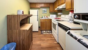 Una cocina compacta con armarios de madera, un refrigerador blanco, un microondas, una estufa y un lavavajillas.