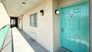 Un pasillo con una puerta verde aguamarina marcada con el número 606, una ventana y una lámpara en la pared.