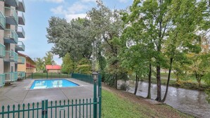 Una piscina rodeada por una cerca verde, con un río y árboles al fondo.