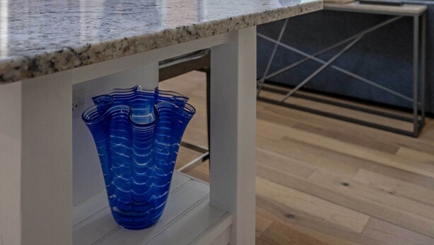 Une cuisine moderne avec un plan de travail en granit, un ventilateur de plafond et un vase bleu posé sur une étagère.