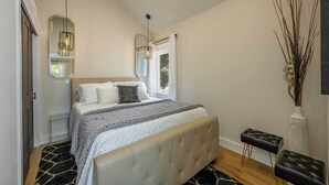 Une chambre avec un grand lit, un miroir, un luminaire suspendu et un vase décoré de branches.