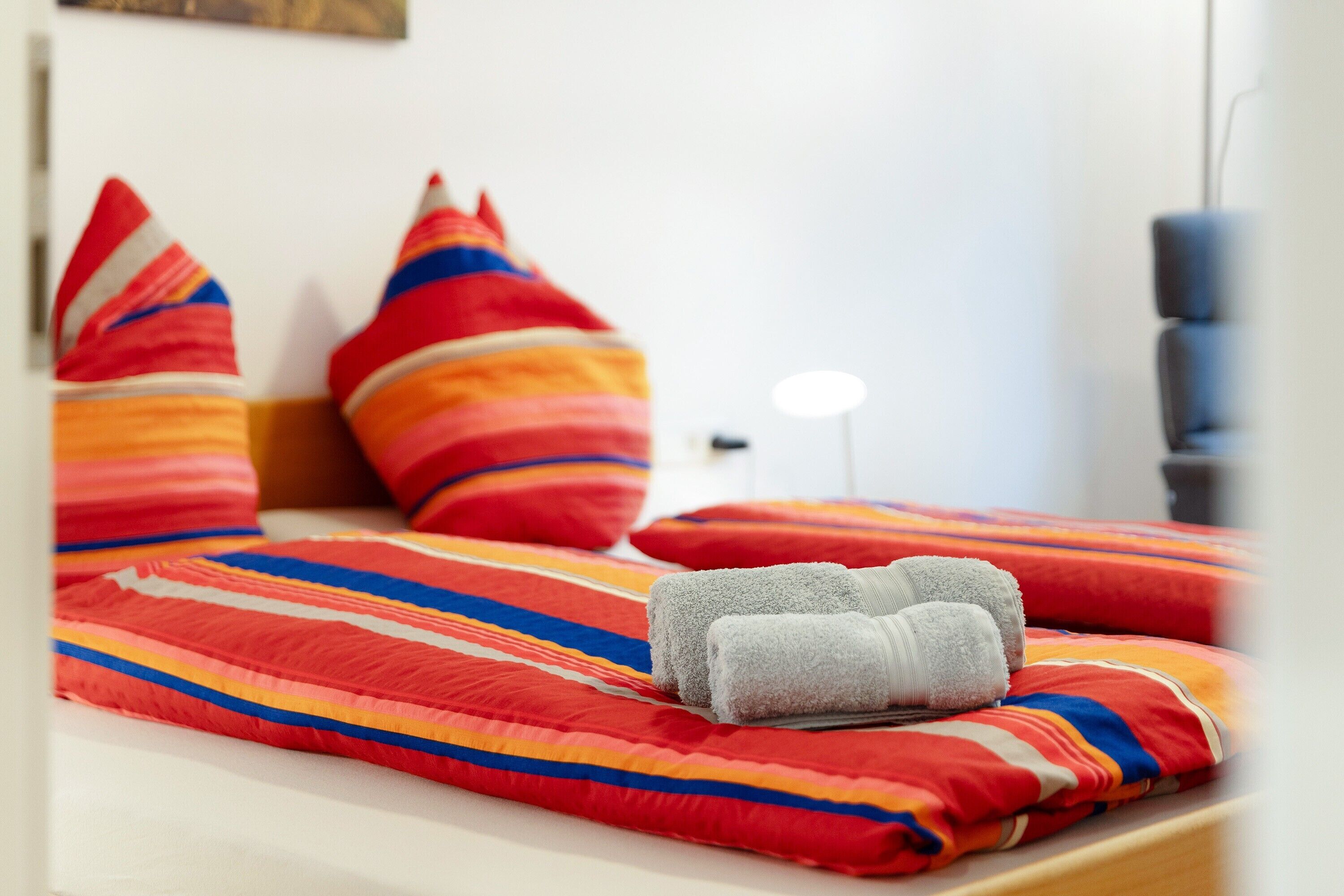 Una cama con una manta a rayas, almohadas y toallas enrolladas.