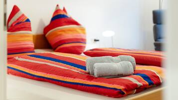 Una cama con una manta a rayas, almohadas y toallas enrolladas.