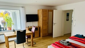 Ein Schlafzimmer mit Bett, Schreibtisch mit Stuhl, Kleiderschrank und Fernseher.