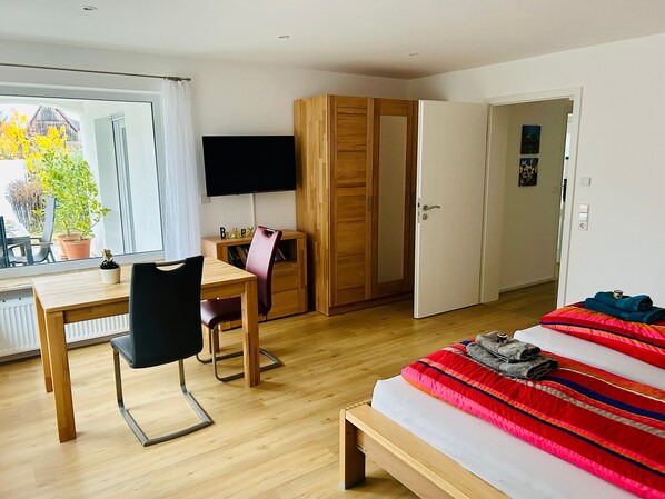 A bedroom with a bed, a desk with a chair, a wardrobe, and a television.