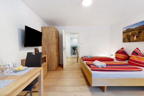 Una habitación de hotel con una cama, un escritorio con silla, un televisor de pantalla plana y un cuadro en la pared.