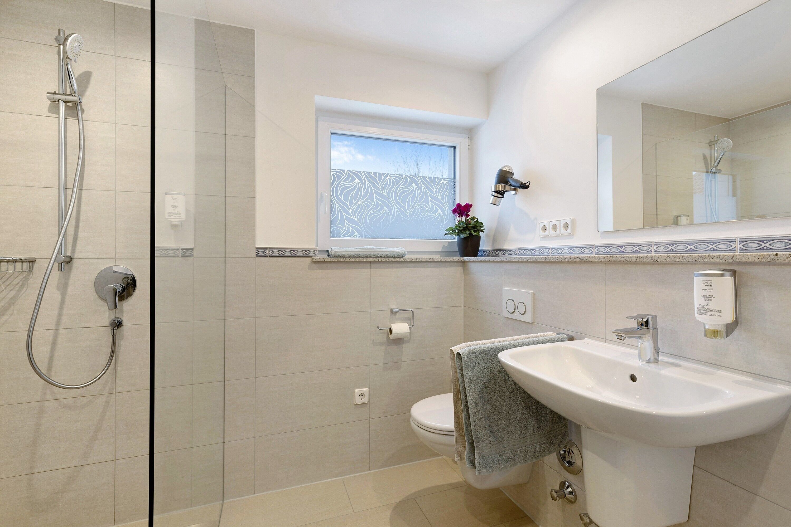 Un bagno con doccia, wc, lavandino e finestra.
