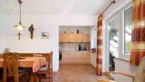 A dining area with a table and chairs, a kitchen with cabinets and appliances, and a window with curtains. - Apartment 'Haus Steigstrasse' with Mountain View, Private Terrace and Wi-Fi (Opfenbach)