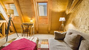 A cozy attic room with a wooden ceiling, a desk with a chair, a lamp, and a sofa with cushions. - Apartment 'Ferienwohnung Tenne' with Shared Garden and Wi-Fi (Vogtsburg)