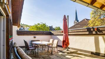 A terrace with a table and chairs, a red umbrella, and a view of a church spire.