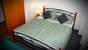 Ein Bett mit Metallgestell, einer grün-weißen Bettdecke und zwei Kissen.