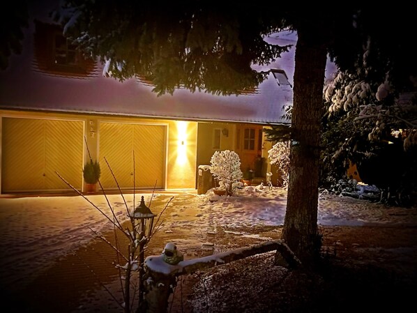 A snow-covered driveway leading to a garage with a lit exterior.
