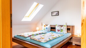 A bedroom with a skylight, a bed with floral bedding, a bedside table with a lamp, and a framed picture on the wall. - Apartment 'Elstar' with Wi-Fi (Stockach)