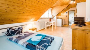 Un dormitorio acogedor en el ático con techo de madera, una cama con ropa de cama estampada, un escritorio y una kitchenette.