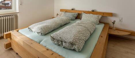 Een houten bed met een lichtgroen matras en bedkussens met een patroon in een kamer met een witte muur en een raam.