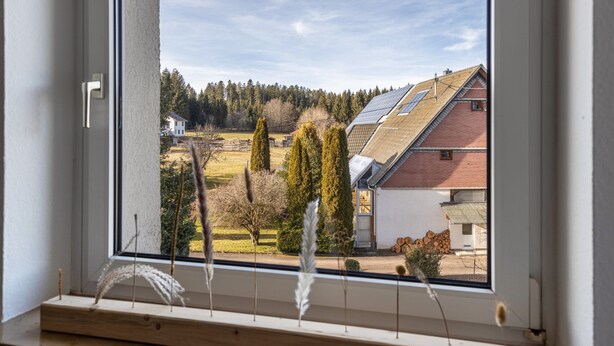 Janela com vista para uma paisagem rural, incluindo casas, árvores e painéis solares nos telhados.