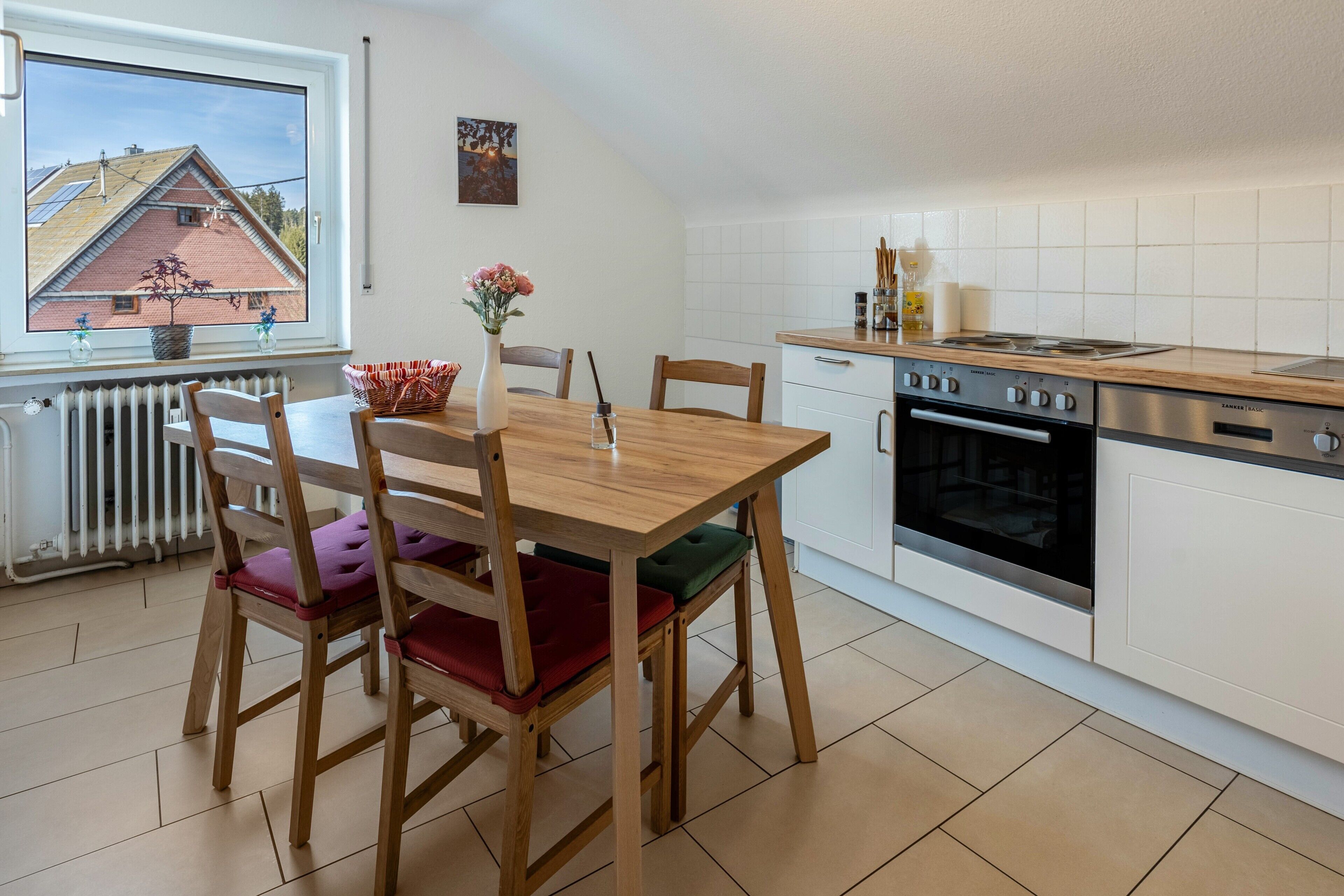 A kitchen with a wooden table, chairs, a stove, and a window with a view of a house.