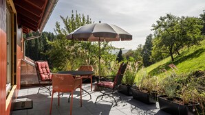 An outdoor patio with a table and chairs, an umbrella, and potted plants. - Haus Wiesenruhe Apartment 1 – Modern & Cozy (Seebach)