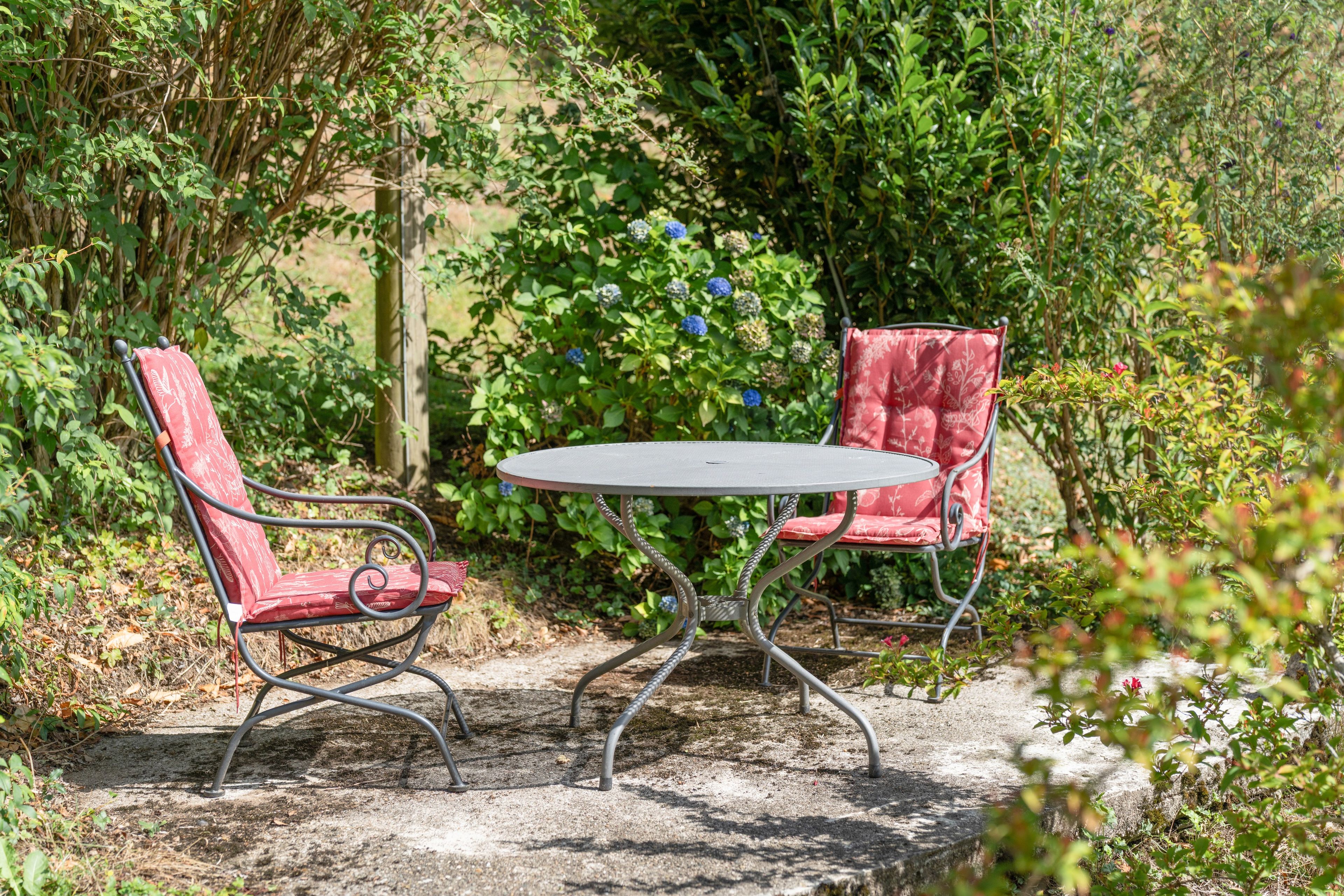 A garden with a round metal table and two red cushioned chairs.