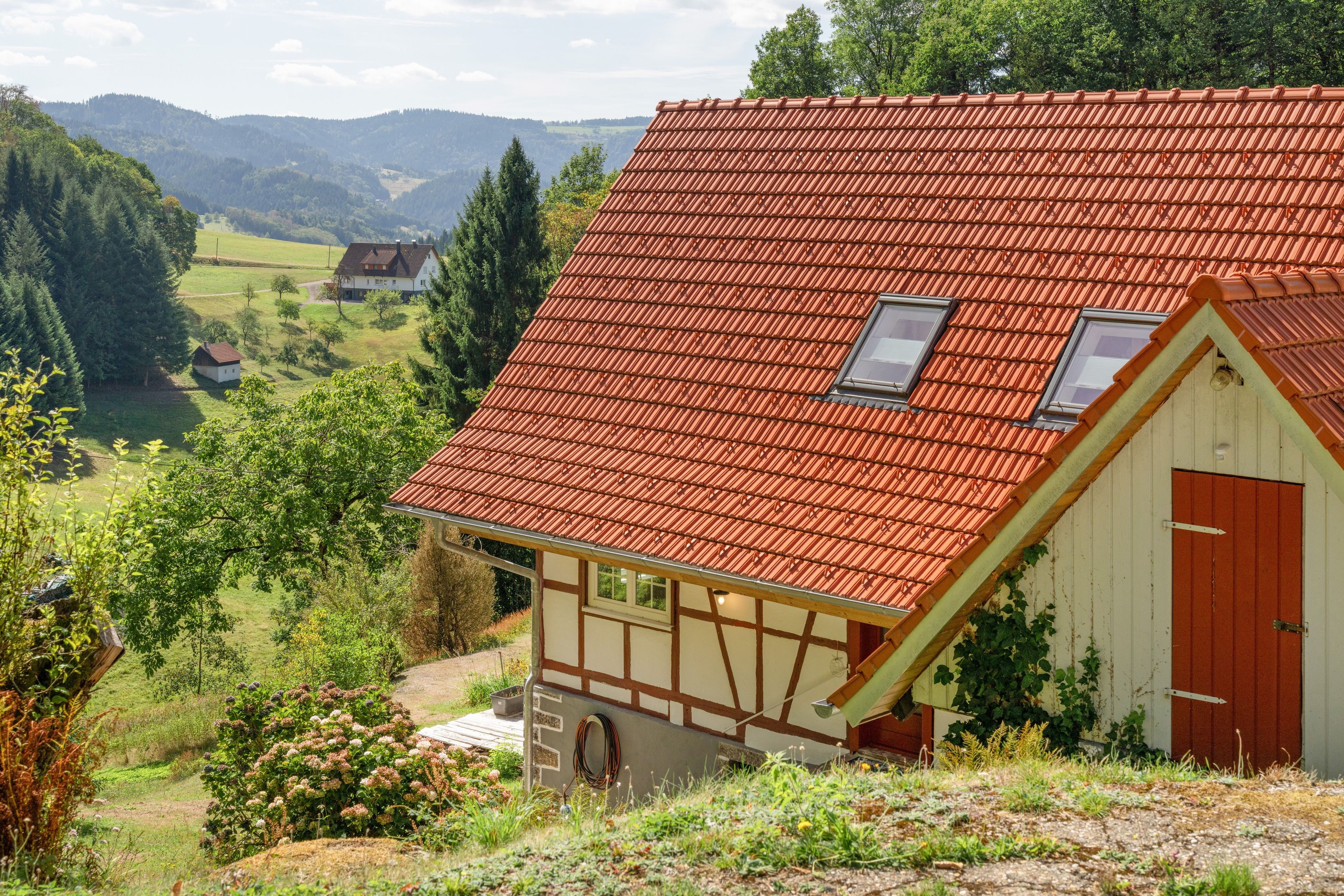 Ein traditionelles Fachwerkhäuschen mit einem geneigten roten Ziegeldach, einem kleinen Fenster und einer Tür.